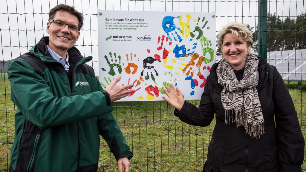 Stephan Riedel (NATURSTROM AG) und Viola Tonn (Bürgermeisterin von Wöbbelin) vor dem mit der Gemeinde gestalteten Schild auf der Einweihungsfeier der Photovoltaikanlage.